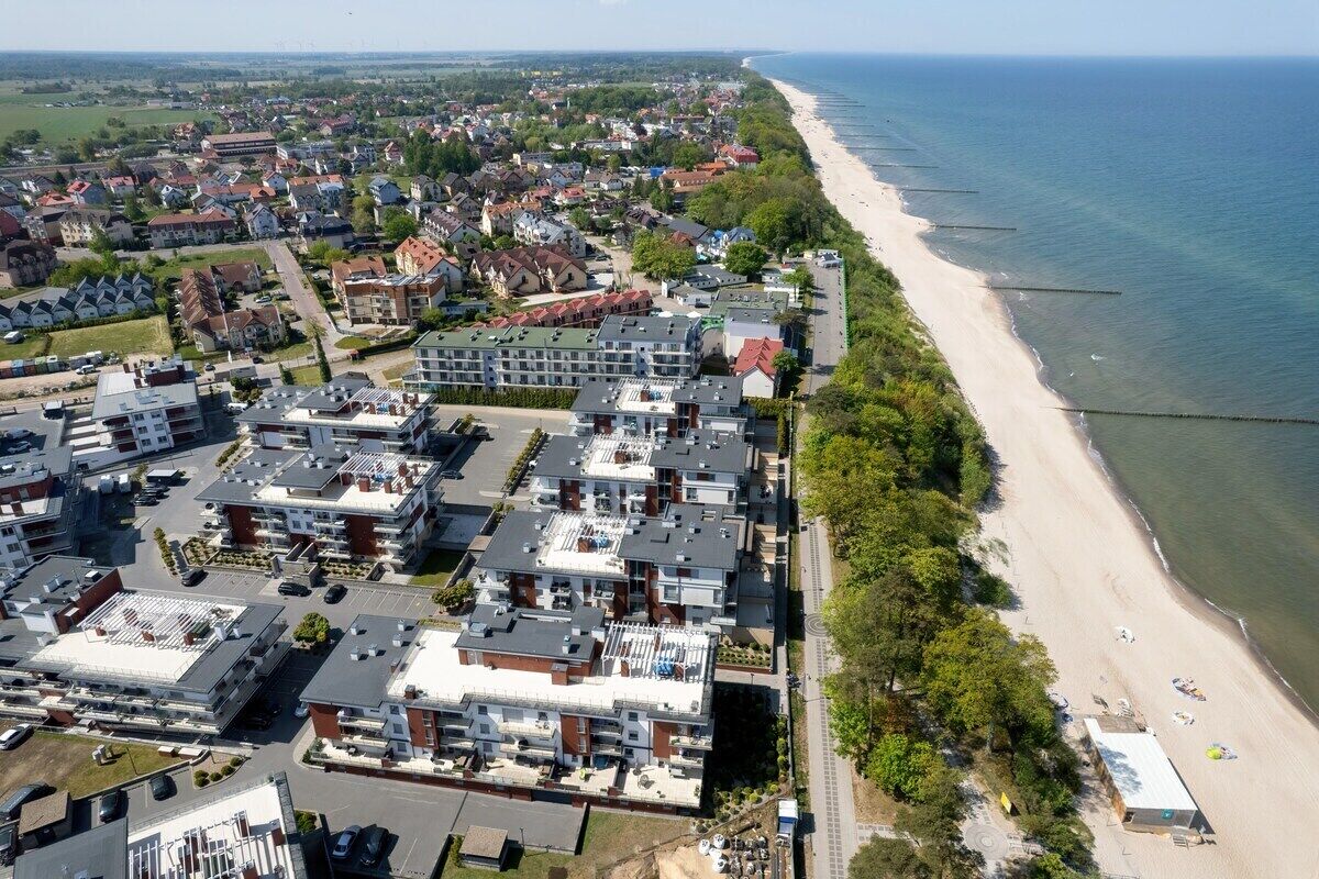 An aerial view of a coastal residential area with modern apartment buildings, a sandy beach, and a clear view of the sea.