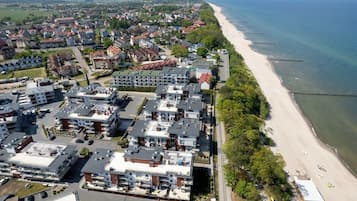 An aerial view of a coastal residential area with modern apartment buildings, a sandy beach, and a clear view of the sea.
