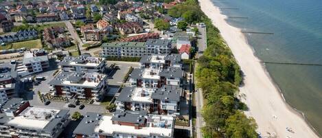An aerial view of a coastal residential area with modern apartment buildings, a sandy beach, and a clear view of the sea.