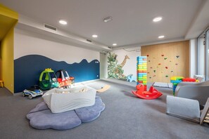 A children's playroom with a climbing wall, soft seating, and toys.
