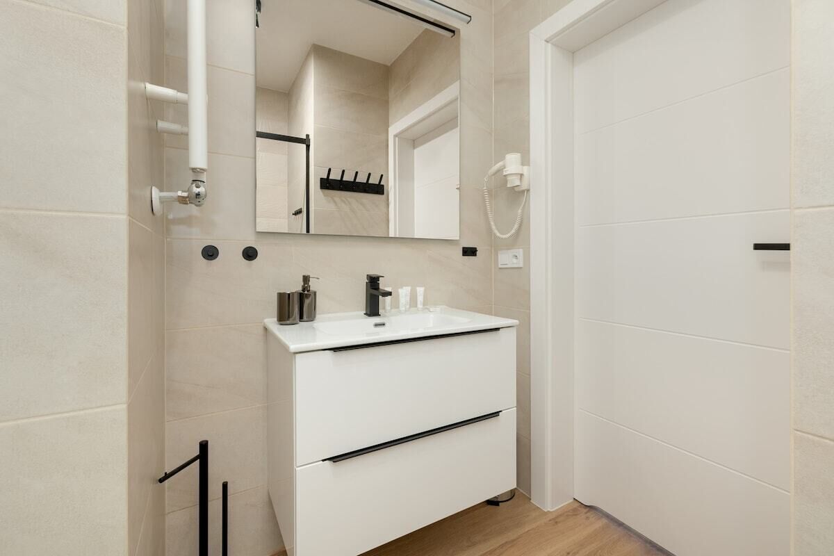 Ein modernes Badezimmer mit einem weißen Waschbecken, einem Spiegel und einem Föhn an der Wand.