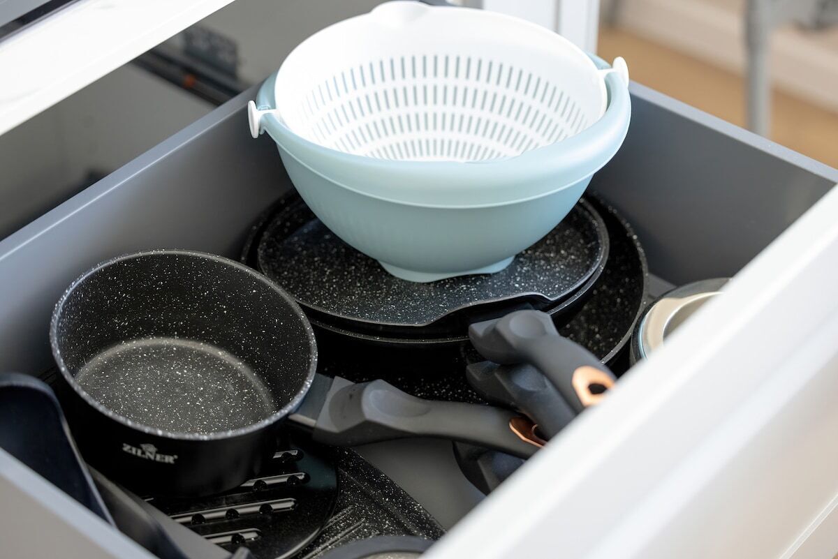 A kitchen drawer with a colander, a frying pan, and a pot.