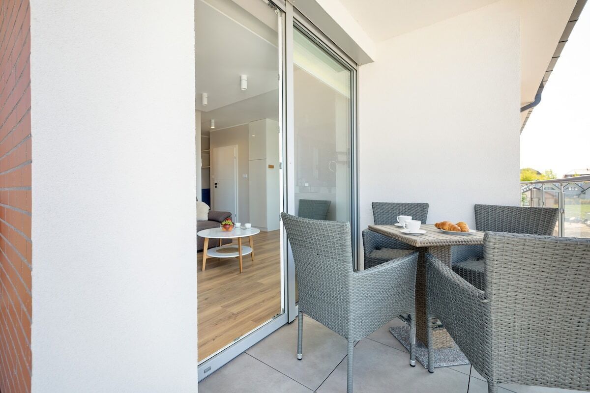 Un balcón con mobiliario de mimbre, una mesa y un ventanal que da a un espacio interior con un sofá y una mesita.