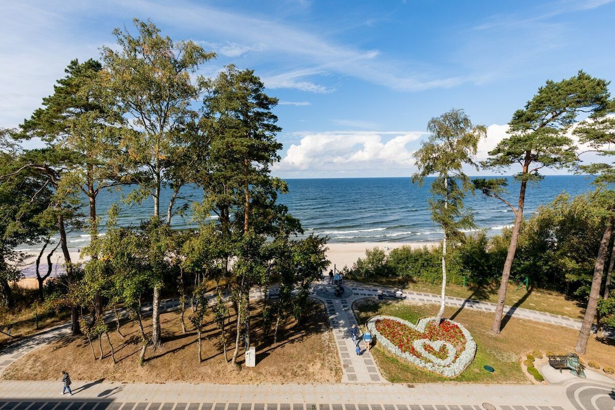 En park vid kusten med träd, en hjärtformad blomsterrabatt och utsikt över havet.