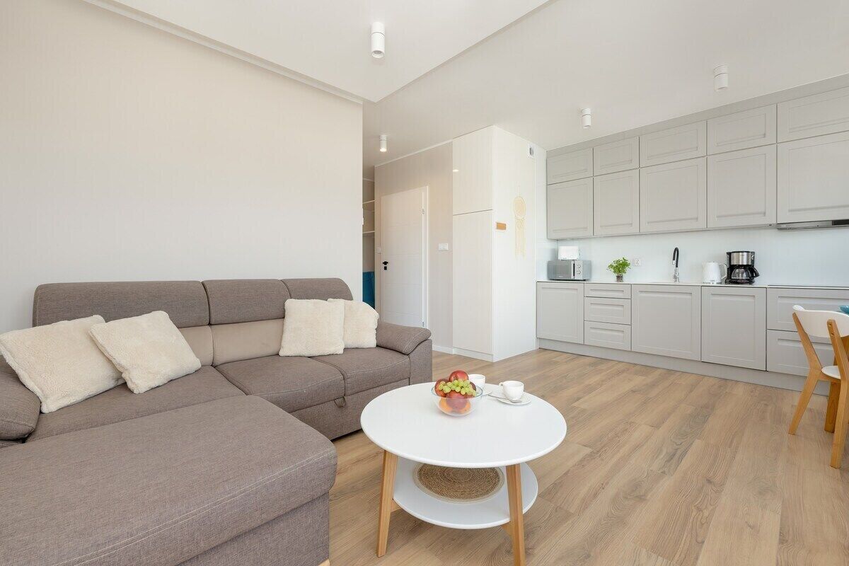 Ein modernes Wohnzimmer mit einer Couch und einem runden Tisch, eine Küche mit weißen Schränken und Holzboden.