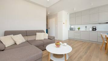 Ein modernes Wohnzimmer mit einer Couch und einem runden Tisch, eine Küche mit weißen Schränken und Holzboden.