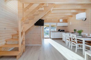 Een houten interieur met een trap, een keuken met witte kasten, en een eethoek met witte stoelen.