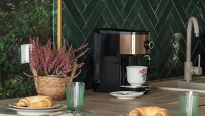 A kitchen with a coffee machine, a potted plant, and a dining area with chairs and plates. - Spacious Apartment | Close to the Beach, Parking. (Mrzeżyno)