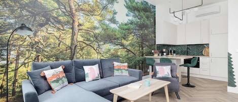 A modern living room with a large sofa, a coffee table, and a view of a forest through a mural.