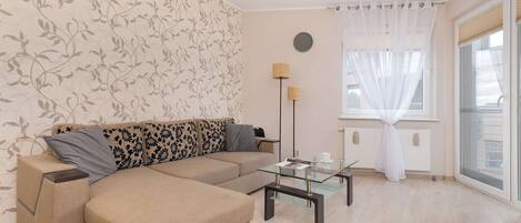 Una sala de estar con un sofá color beige, una mesa de centro de vidrio y un papel tapiz estampado.