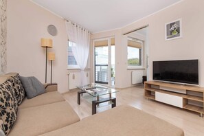 En moderne stue med sofa, sofabord i glas, tv-møbel og gulvlampe.