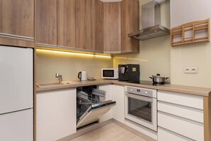 Une cuisine moderne dotée de meubles en bois, d’un lave-vaisselle, d’un four, d’un four à micro-ondes et d’une bouilloire.