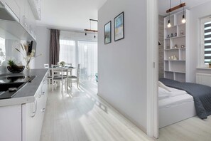 Eine moderne Küche mit weißen Schränken, ein Essbereich mit Tisch und Stühlen, ein Bett mit grauer Decke und eine Wand mit zwei gerahmten Bildern.