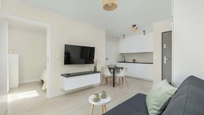 Ein modernes Wohnzimmer mit einer Couch, einem kleinen Tisch mit Tassen, einem an der Wand befestigten Fernseher und einem Essbereich mit Stühlen und einem Tisch.