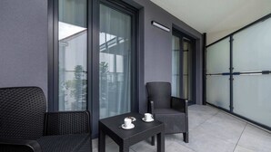 A balcony with two wicker chairs and a small table, a glass door, and a view of the outside.