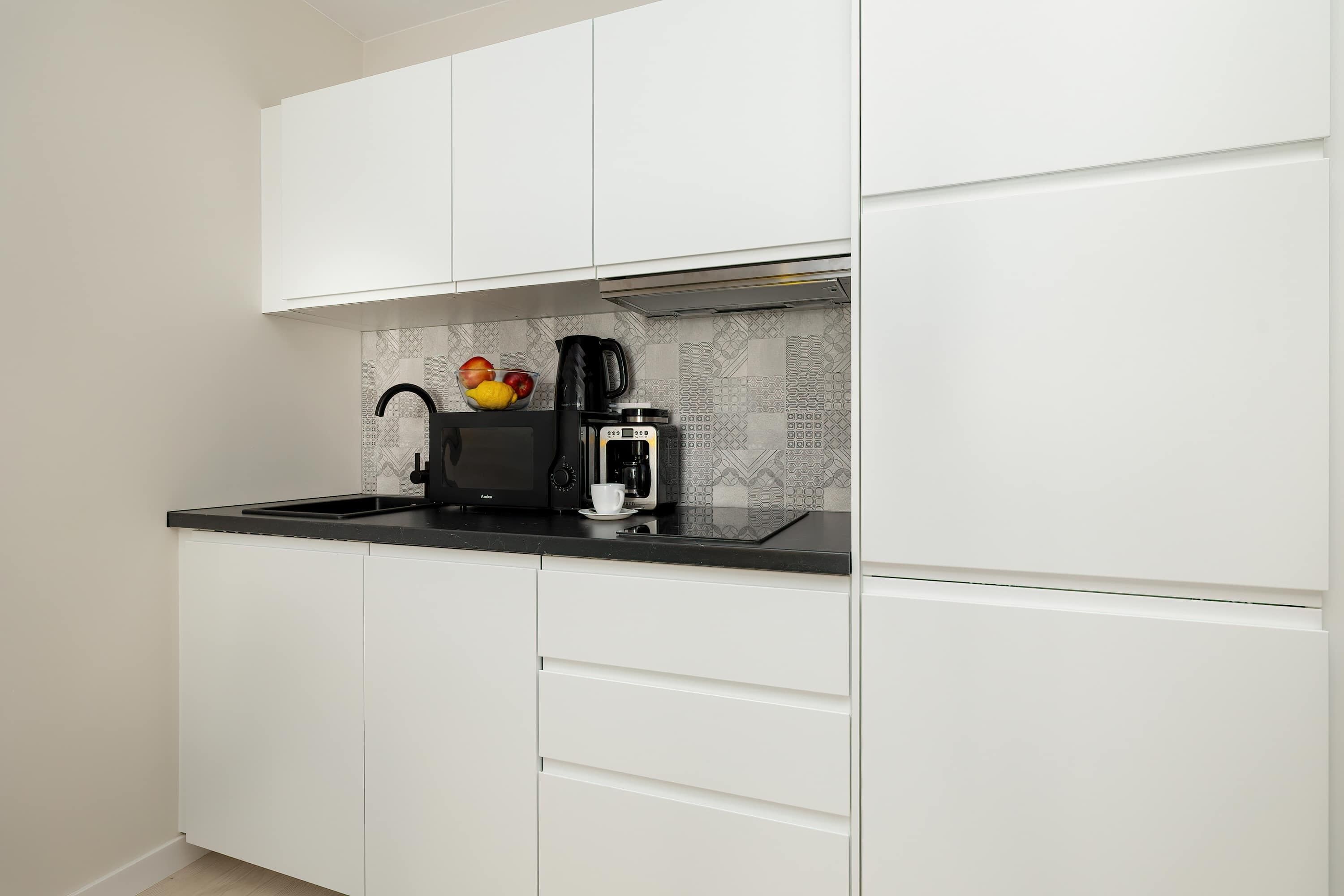 Een moderne keuken met witte kasten, een zwart aanrecht en een koffiezetapparaat.