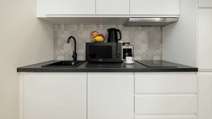 A kitchen with white cabinets, a black countertop, a microwave, a coffee maker, and a fruit bowl.