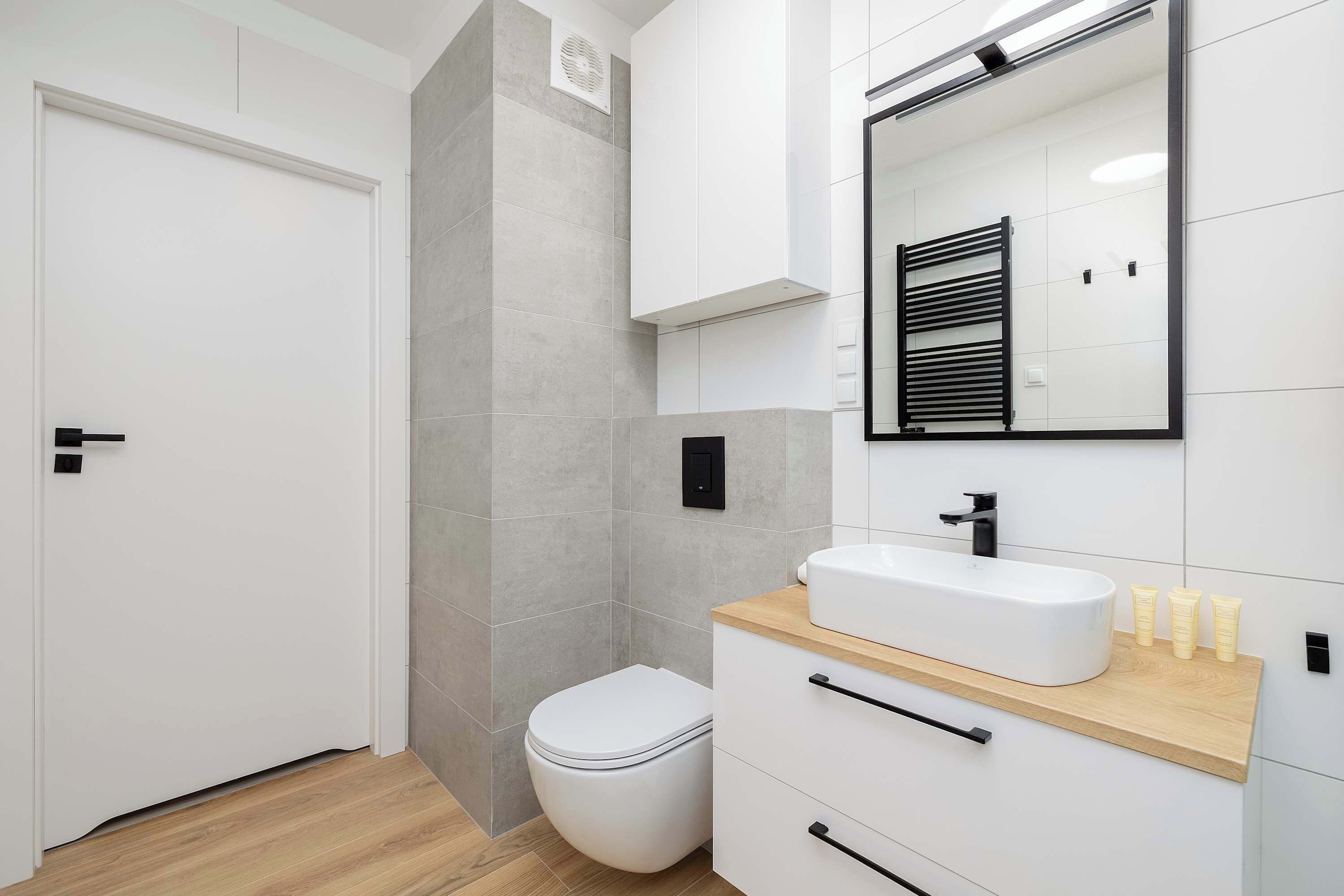 Une salle de bain moderne avec des toilettes blanches, un meuble-lavabo en bois, un grand miroir et un porte-serviettes.