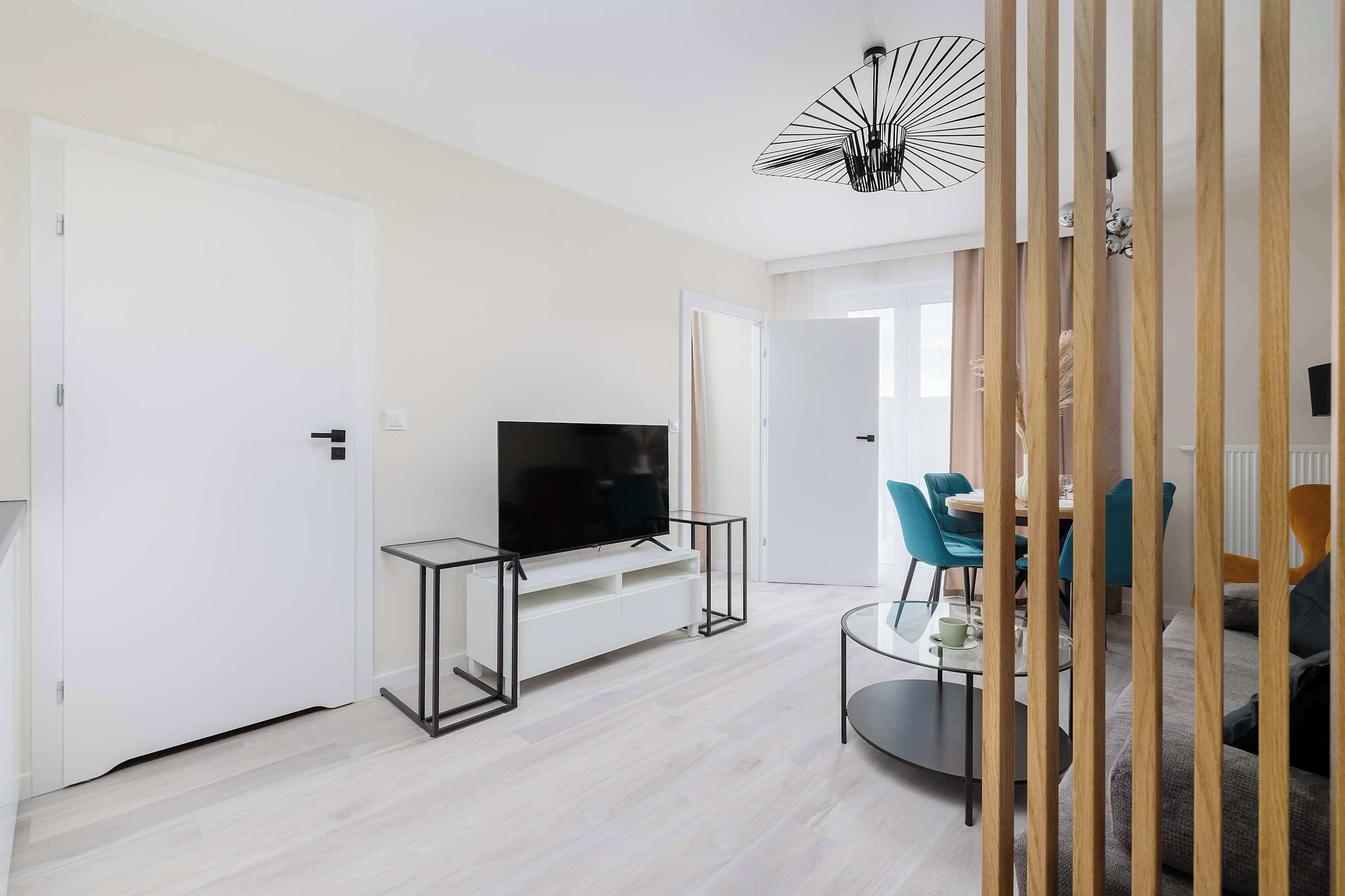 Una sala moderna con una televisión de pantalla plana sobre una mesa de vidrio, un comedor con sillas, y un sofá.