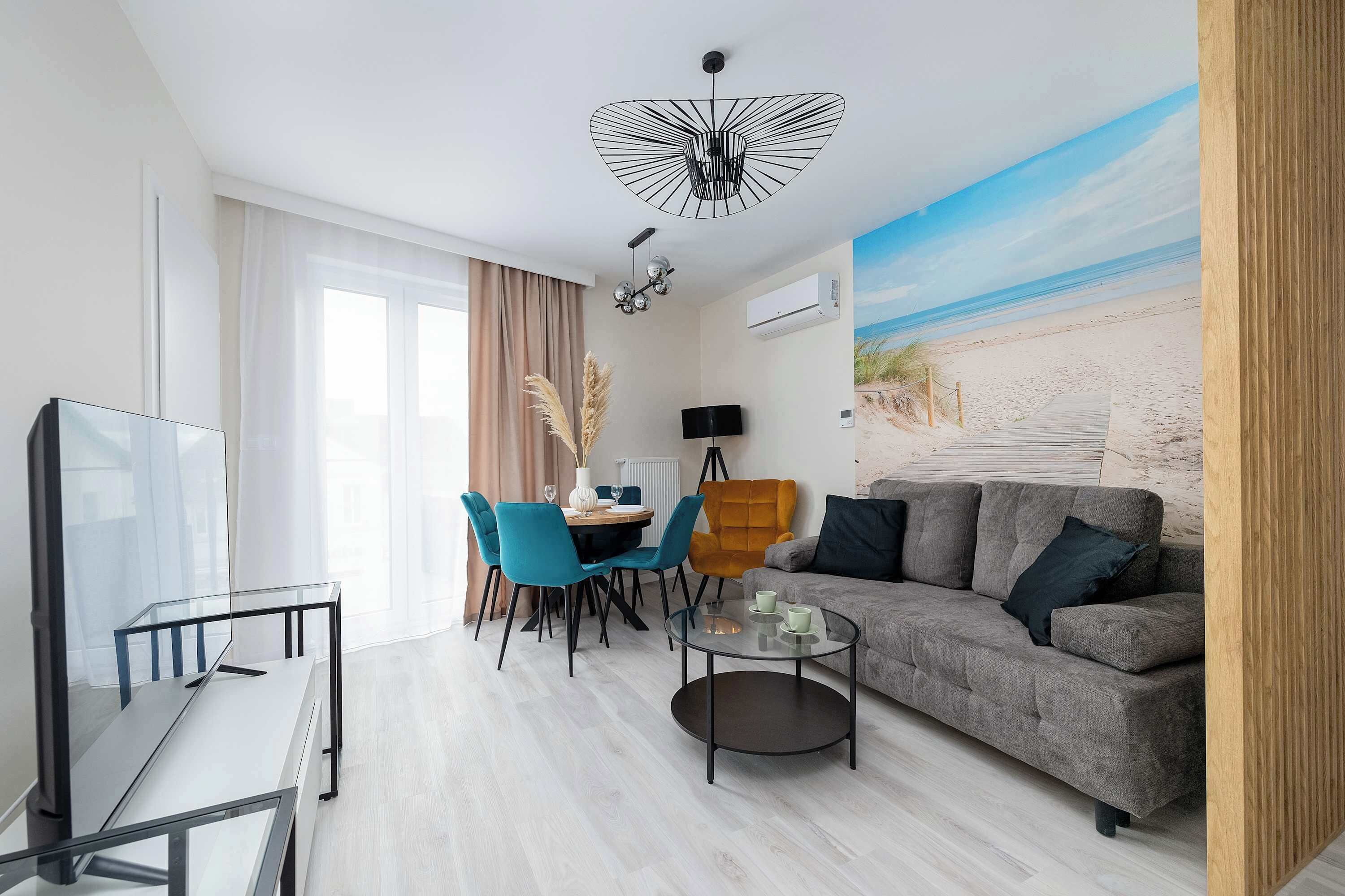 Un salon moderne avec un canapé gris, une table basse en verre et un coin repas avec des chaises bleues et orange.