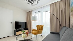 Un salon moderne avec un téléviseur à écran plat, une table basse ronde en verre, un fauteuil jaune et un canapé gris.