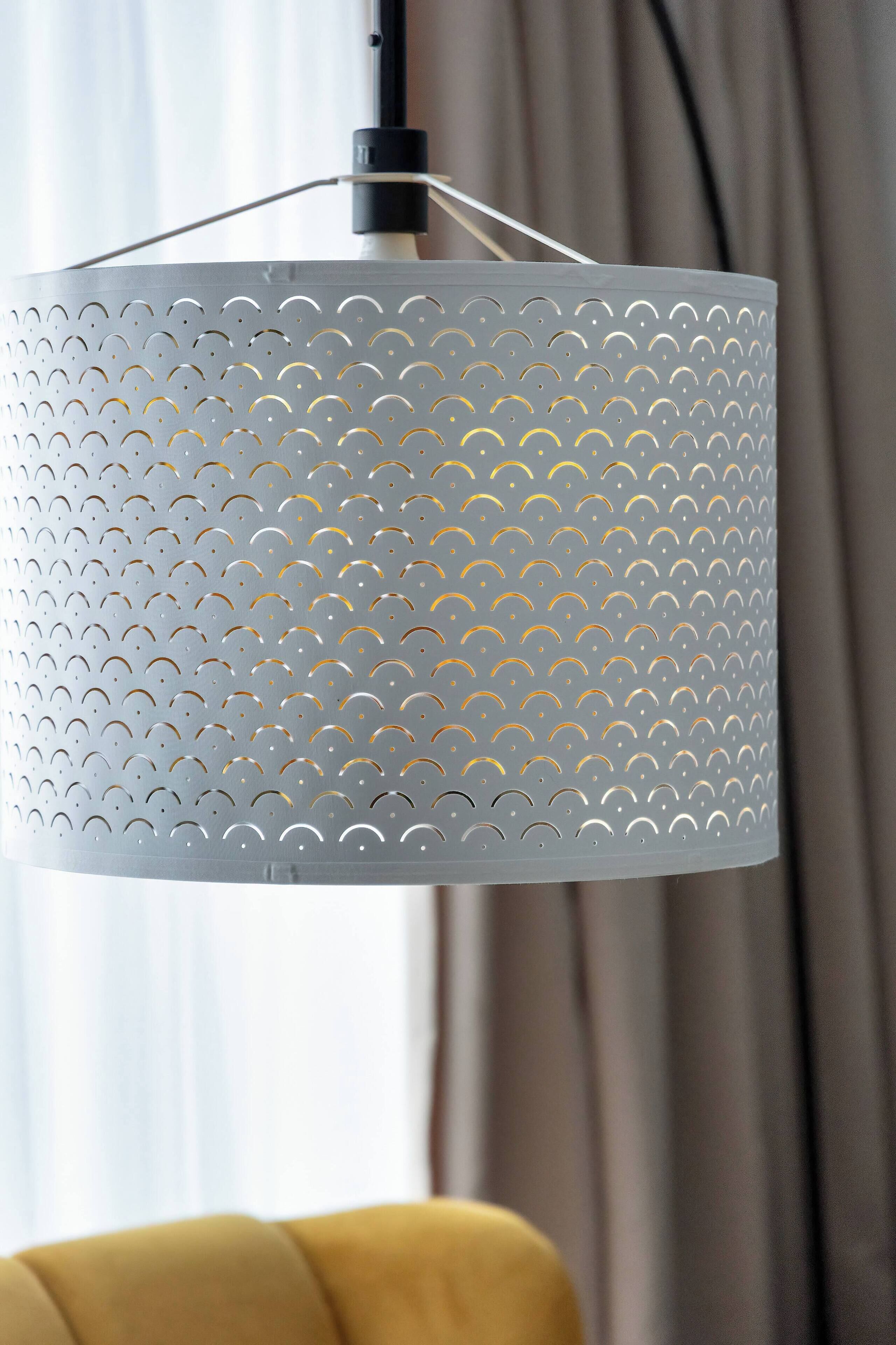 Una lámpara cilíndrica gris con perforaciones que cuelga de un accesorio de techo.