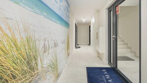 Un couloir orné d’une fresque représentant une plage, un tapis bleu avec le mot « AMAR » inscrit dessus, et un escalier menant à une pièce.