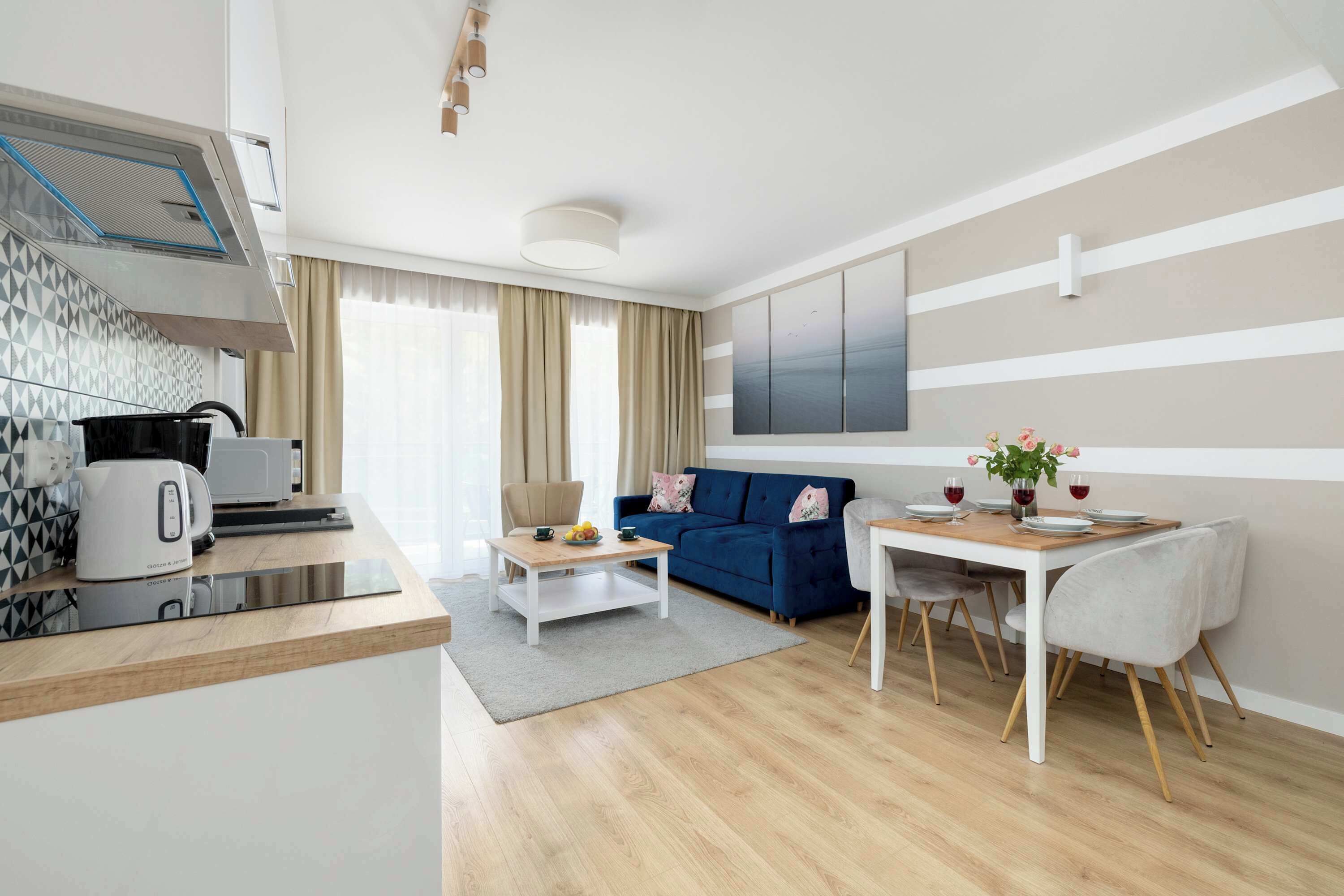 A modern living room with a sofa, a dining table with chairs, a coffee table, and a kitchen area with a kettle and toaster.