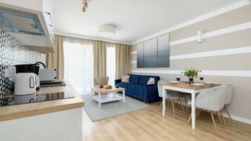 A modern living room with a sofa, a dining table with chairs, a coffee table, and a kitchen area with a kettle and toaster.