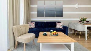 Una sala de estar moderna con un sofá color beige, una mesa de centro de madera con fruta y un comedor con una mesa blanca y sillas grises.