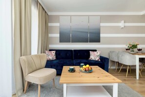 Een moderne woonkamer met een beige bank, een houten salontafel met fruit, en een eetgedeelte met een witte tafel en grijze stoelen.