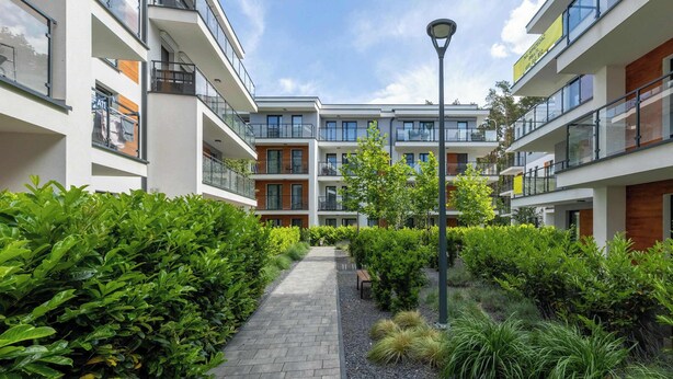 Un moderno complejo de apartamentos con un patio central, que cuenta con un sendero pavimentado, abundante vegetación y un farol.