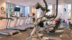 Ett gym med flera löpband och crosstrainers, stora fönster och en klocka på väggen.