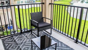 Ein Balkon mit einem schwarzen Korbsessel und einem kleinen Tisch, mit Blick auf eine Rasenfläche und ein Gewässer.