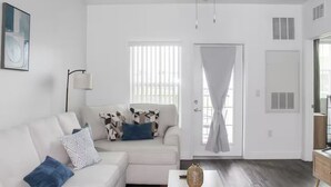 Ein modernes Wohnzimmer mit einem weißen Sofa, gemusterten Kissen, einer Stehlampe und einem Deckenventilator.