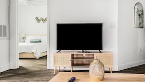 Ein modernes Wohnzimmer mit einem Flachbildfernseher auf einem Holz-TV-Möbel, einer Fernbedienung und einer dekorativen Vase auf einem Couchtisch.