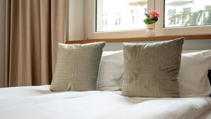 Ein ordentlich bezogenes Bett mit zwei Kissen und einer Vase mit einer Blume auf der Fensterbank.