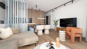 A modern living room with a sofa, a coffee table, a TV, and a kitchen area in the background.