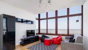 A modern living room with a large window, a flat-screen TV, a grey sofa, red bean bag chairs, and a black entertainment unit.