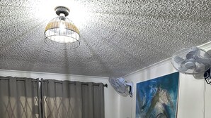 A living room with a black sofa, a red rug, a white tiled floor, a ceiling fan, and a painting on the wall.