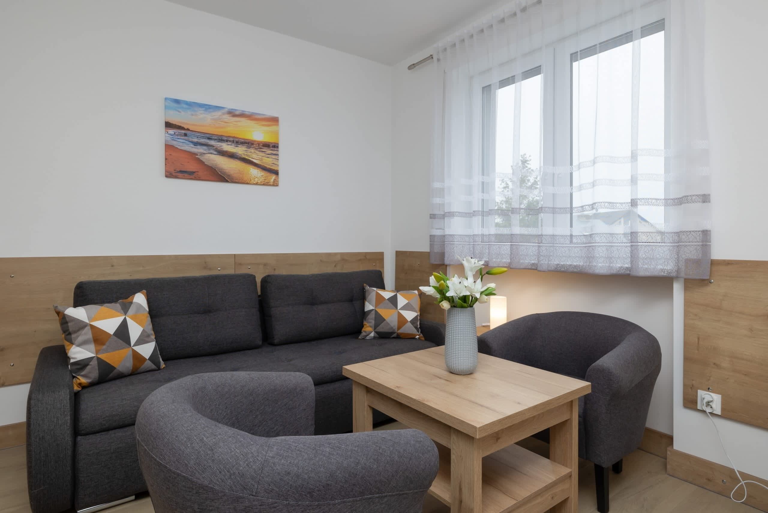 A modern living room with a sofa, two armchairs, a wooden coffee table, and a painting on the wall.