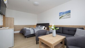 A modern room with a bed, two sofas, a small table, a TV, and a painting on the wall.