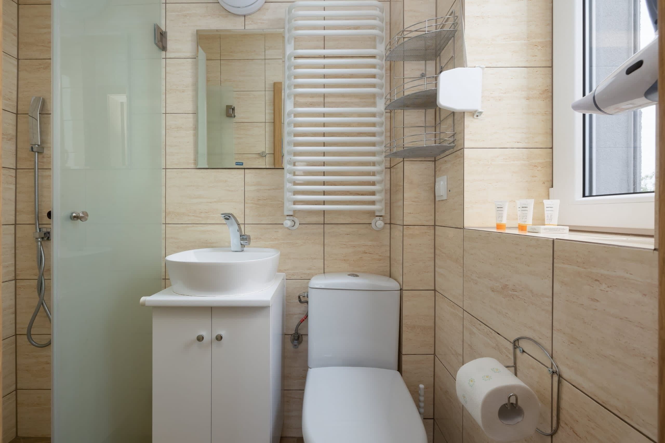 A bathroom with a toilet, sink, shower, and a toilet paper holder.
