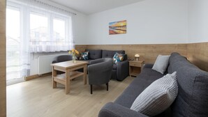 Una sala de estar moderna con un sofá, un sillón y una mesa, un cuadro en la pared y vistas a través de amplias ventanas.