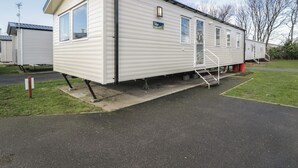A single-story mobile home with a flat roof, a front porch, and a small staircase leading to the entrance. - Lido Silver Plus 111 (Prestatyn)