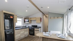A compact kitchen with wooden cabinets, a black refrigerator, a microwave, and a stove. - Lido Silver Plus 111 (Prestatyn)