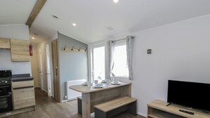 A modern kitchen with wooden cabinets, a stove, and a dining area with a table set for four. - Lido Silver Plus 111 (Prestatyn)