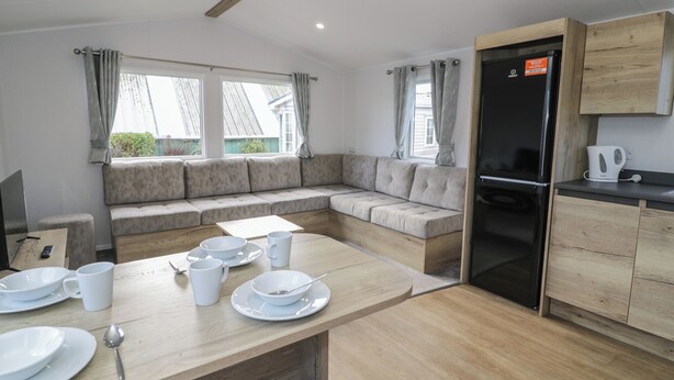 A modern kitchen with a wooden countertop, a built-in oven, and a seating area with a sofa and windows. - Lido Silver Plus 111 (Prestatyn)