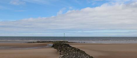 A beach with a rocky breakwater and a clear sky.