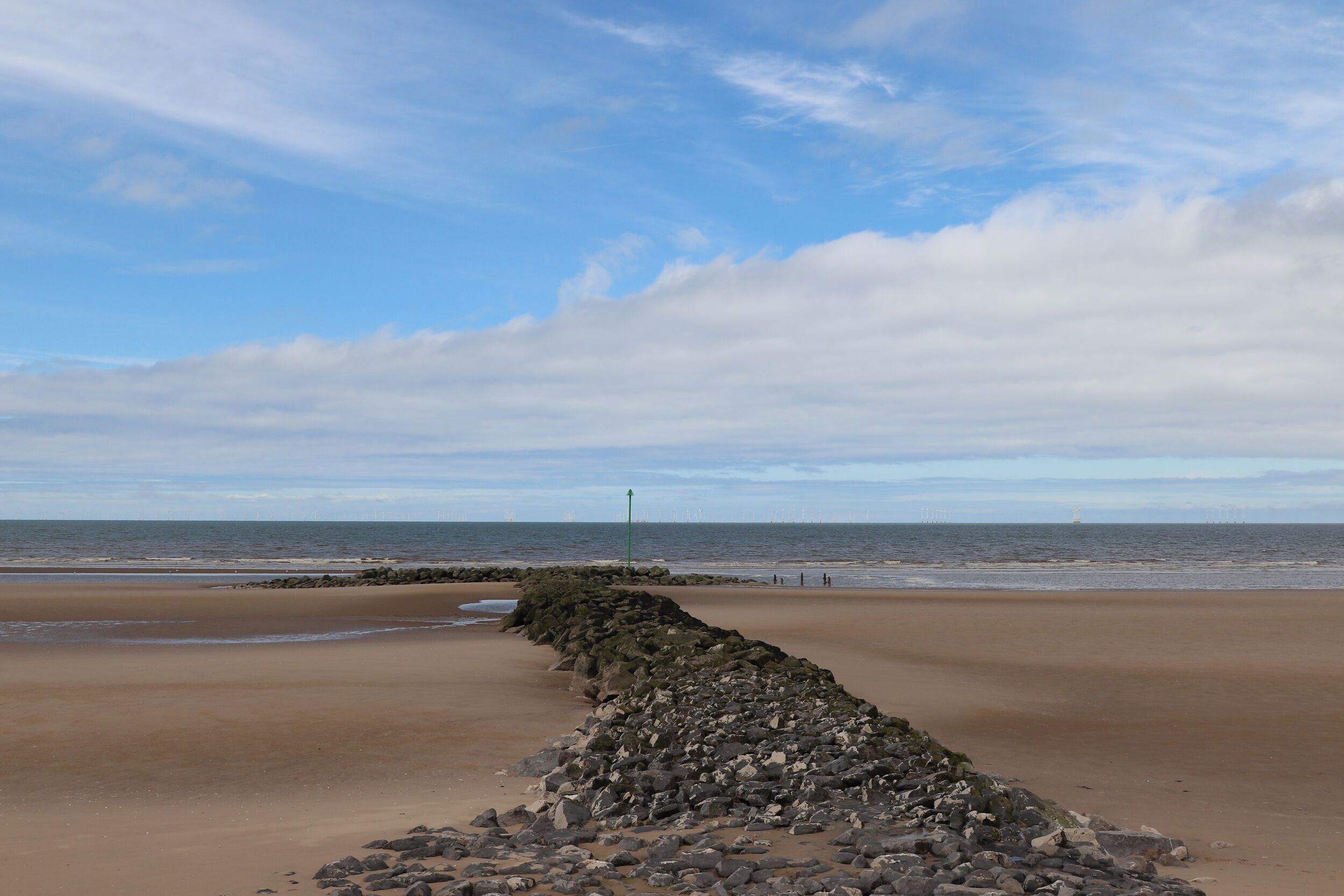 A beach with a rocky breakwater and a clear sky.